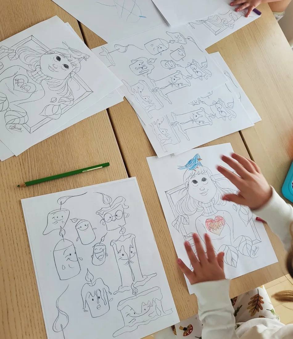 Des mains d’enfant posées sur des coloriages de Laura étalés sur une table