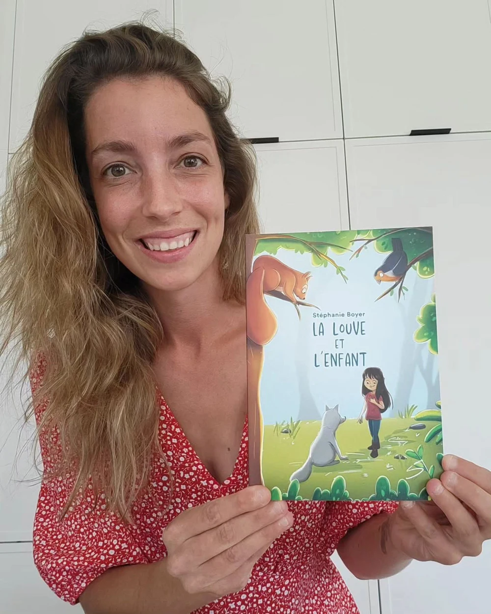 Laura Vandal sourit en tenant le livre La louve et l’enfant, qu’elle a illustré
